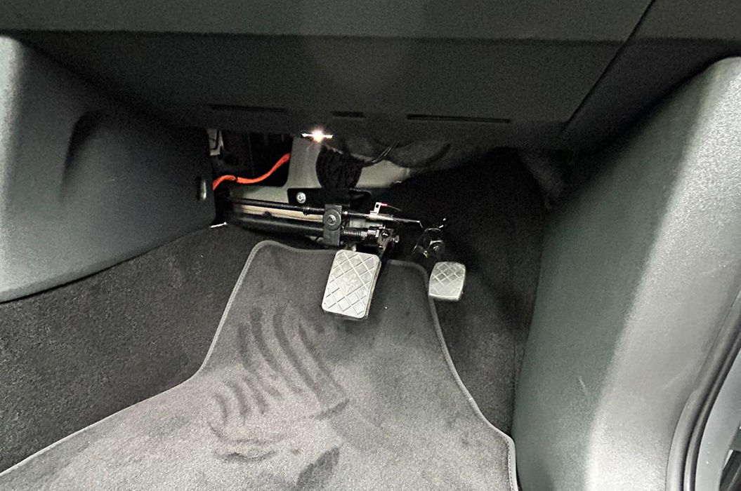 Zwei silberne Pedale im Fußraum eines Autos auf schwarzem Teppichboden